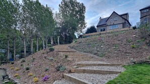 Un barrio residencial con un jardín inclinado, escalones de madera y una casa al fondo.