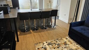 Una cocina moderna con una isla central, un área de comedor con taburetes de bar, un sofá azul y una alfombra estampada.