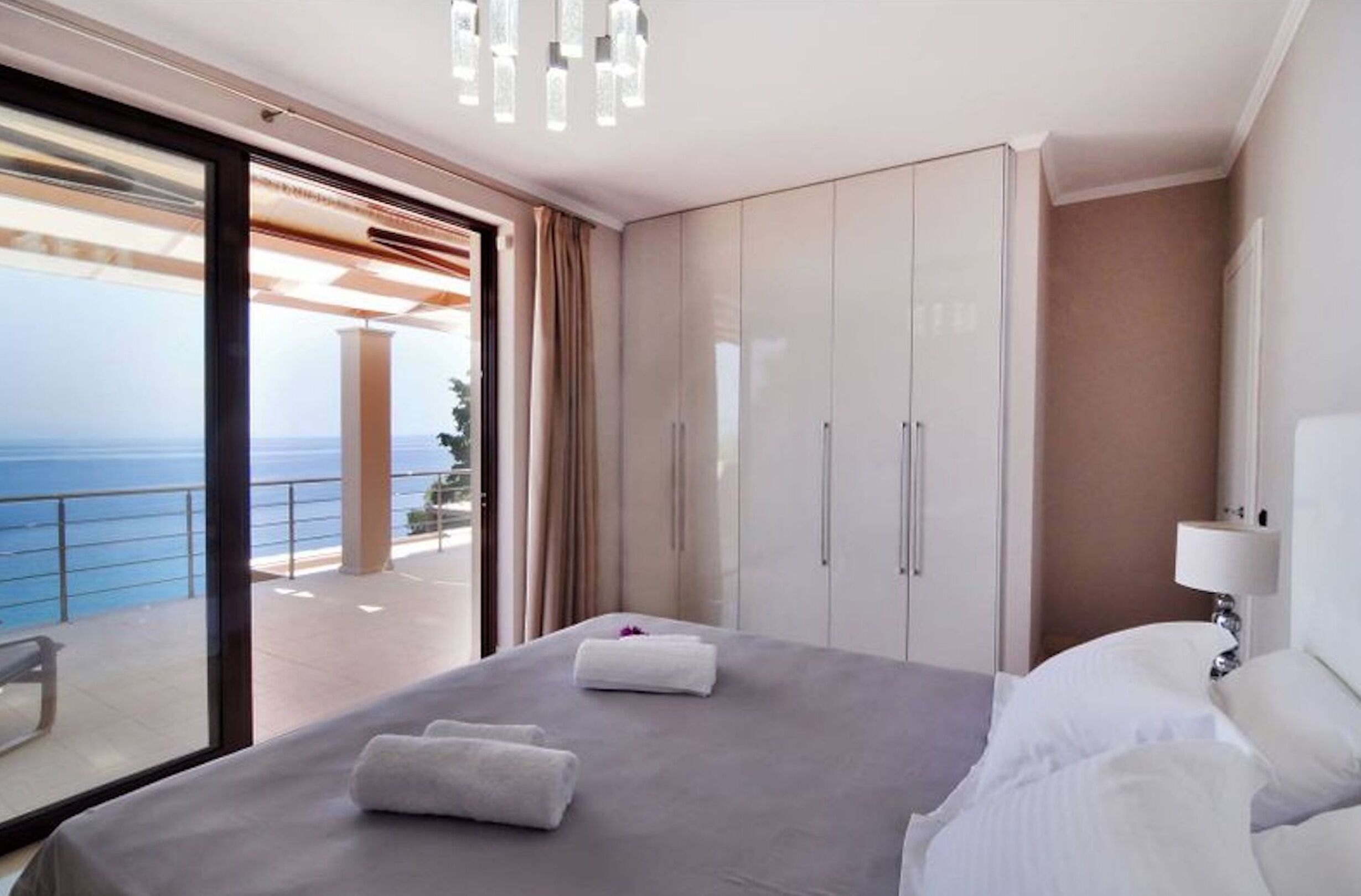 A bedroom with a bed, a nightstand, a large wardrobe, and a balcony with a view of the sea.