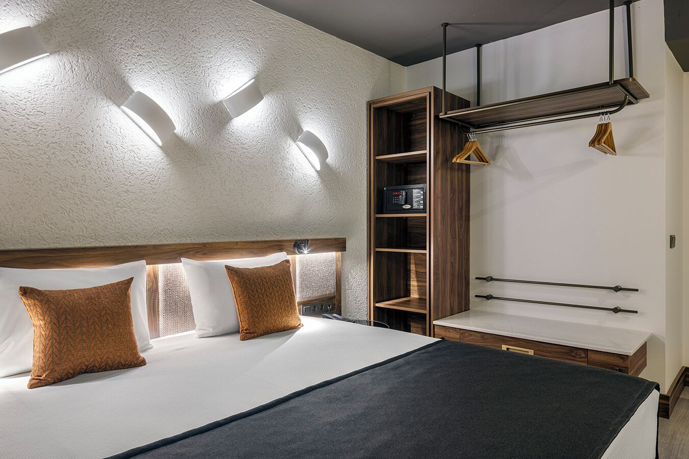 A modern hotel room with a large bed, a wooden wardrobe, and a built-in bench.