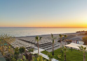 A beachside hotel with rows of sun loungers, a pool area, and a view of the ocean at sunset. - Kaia Coracesium (Alanya)
