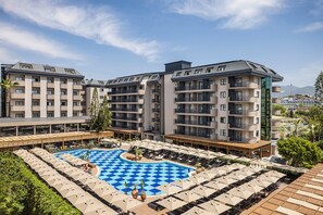 A hotel with multiple floors, a central pool with a checkered pattern, and outdoor seating areas with umbrellas. - Kaia Coracesium (Alanya)