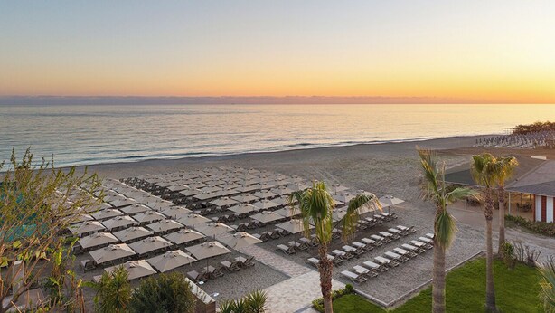 A beachside hotel with rows of sun loungers and umbrellas, a pool area, and a view of the ocean. - Kaia Coracesium (Alanya)