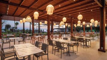Un espace de restauration en plein air avec des tables et des chaises, des poutres en bois et des lampes suspendues.