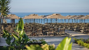 A beachside seating area with rows of chairs and umbrellas, a clear view of the ocean, and a pathway leading to the beach. - Kaia Coracesium (Alanya)