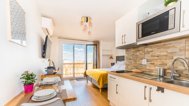 Eine moderne Küche mit Mikrowelle, Spüle und einer Holz Arbeitsplatte. Es gibt einen Essbereich mit einem Tisch für zwei Personen und einem Blumentopf.
