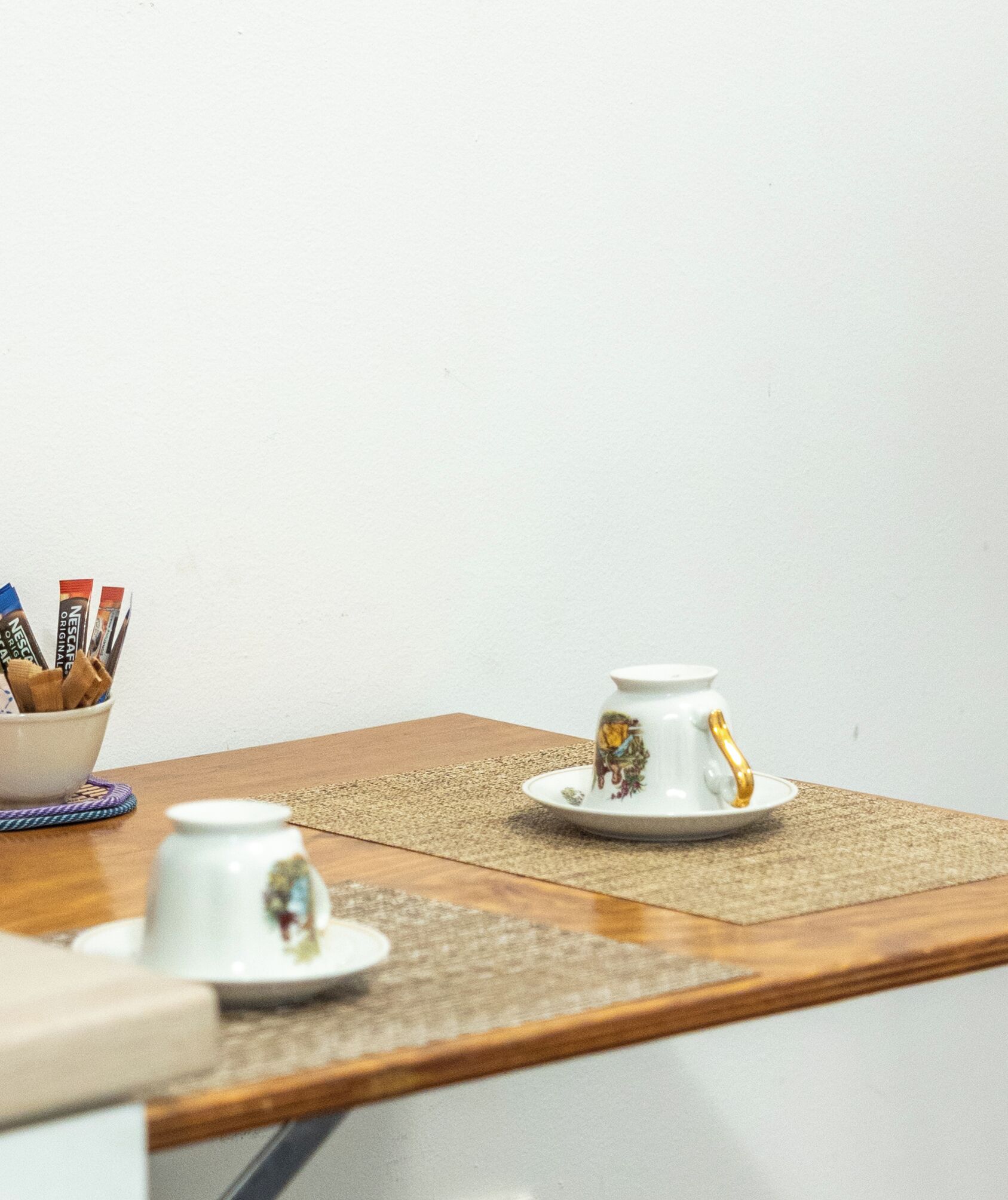 Un tavolo con un bollitore bianco, una tazza e una ciotola con bustine di caffè Nescafe Original.