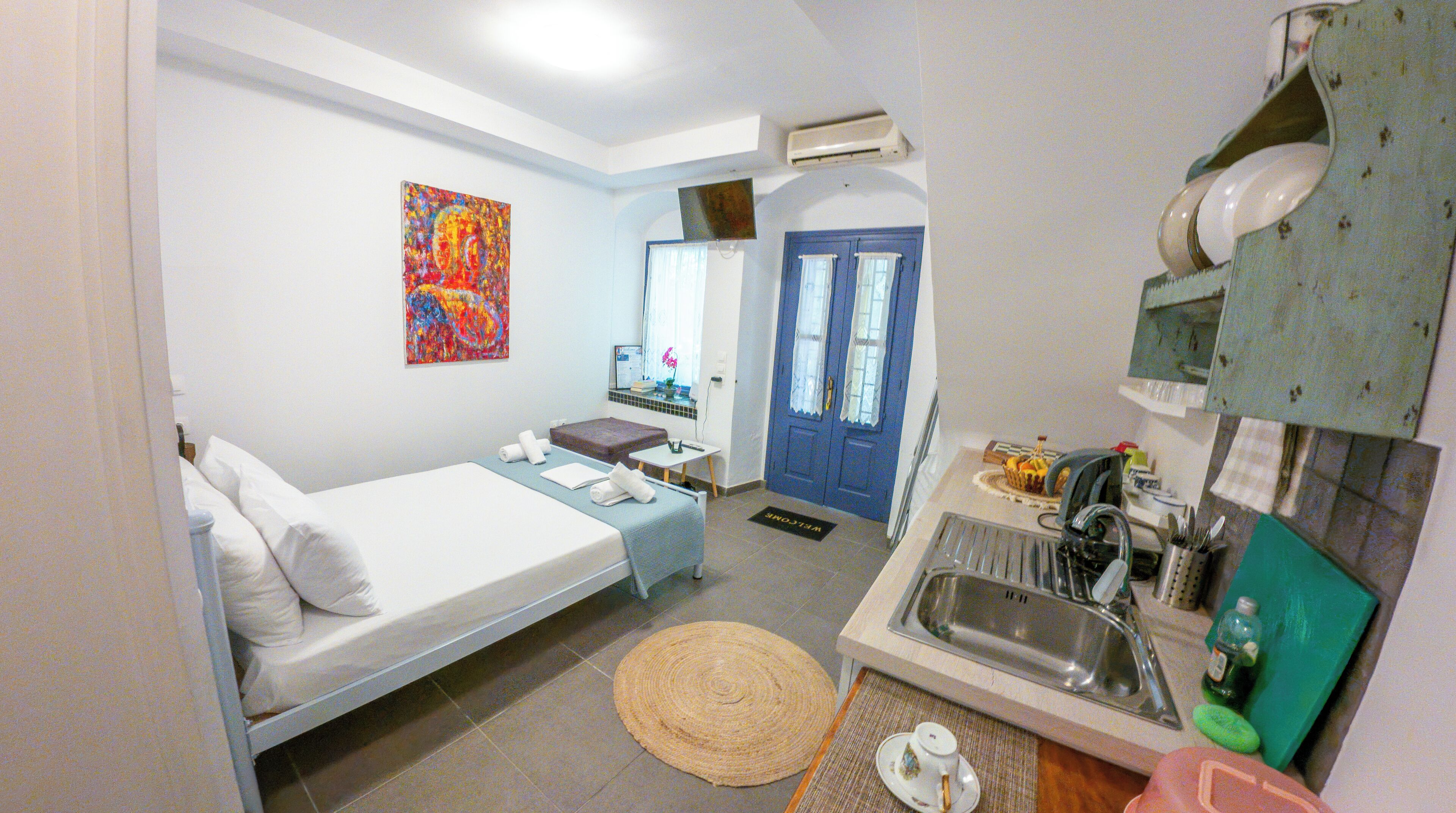 Habitación de hotel pequeña con cama, un escritorio, un lavabo y un cuadro de colores en la pared.