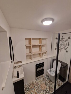A bathroom with a toilet, a shelf unit, a radiator, and a decorative compass wall art. - 2 Bed Annex Sleeps 6, 7 Min Drive From the Beach! (Truro)