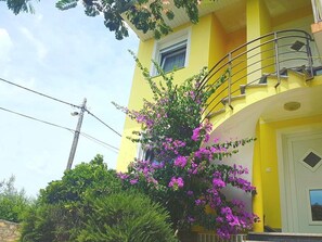 A yellow building with a balcony, surrounded by greenery and purple flowers. - Floral Apartments Yazzy 1 (Novalja)