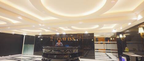 A hotel lobby with a reception desk, a large mirror, and a modern ceiling design.