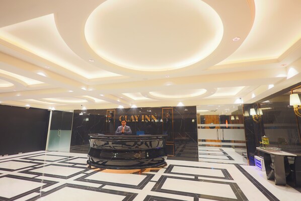 Un vestíbulo de hotel con una recepción, un espejo grande y un diseño moderno de techo.