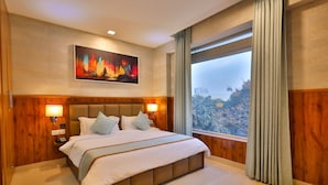 A hotel room with a large bed, wooden paneling, a painting on the wall, and a view of trees through the window. - Clay Inn Hotel Gurugram (Gurugram)