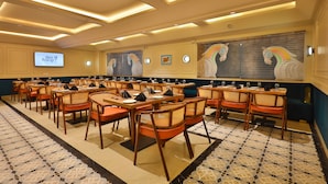 A conference room with multiple tables and chairs, a large screen, and decorative wall art. - Clay Inn Hotel Gurugram (Gurugram)