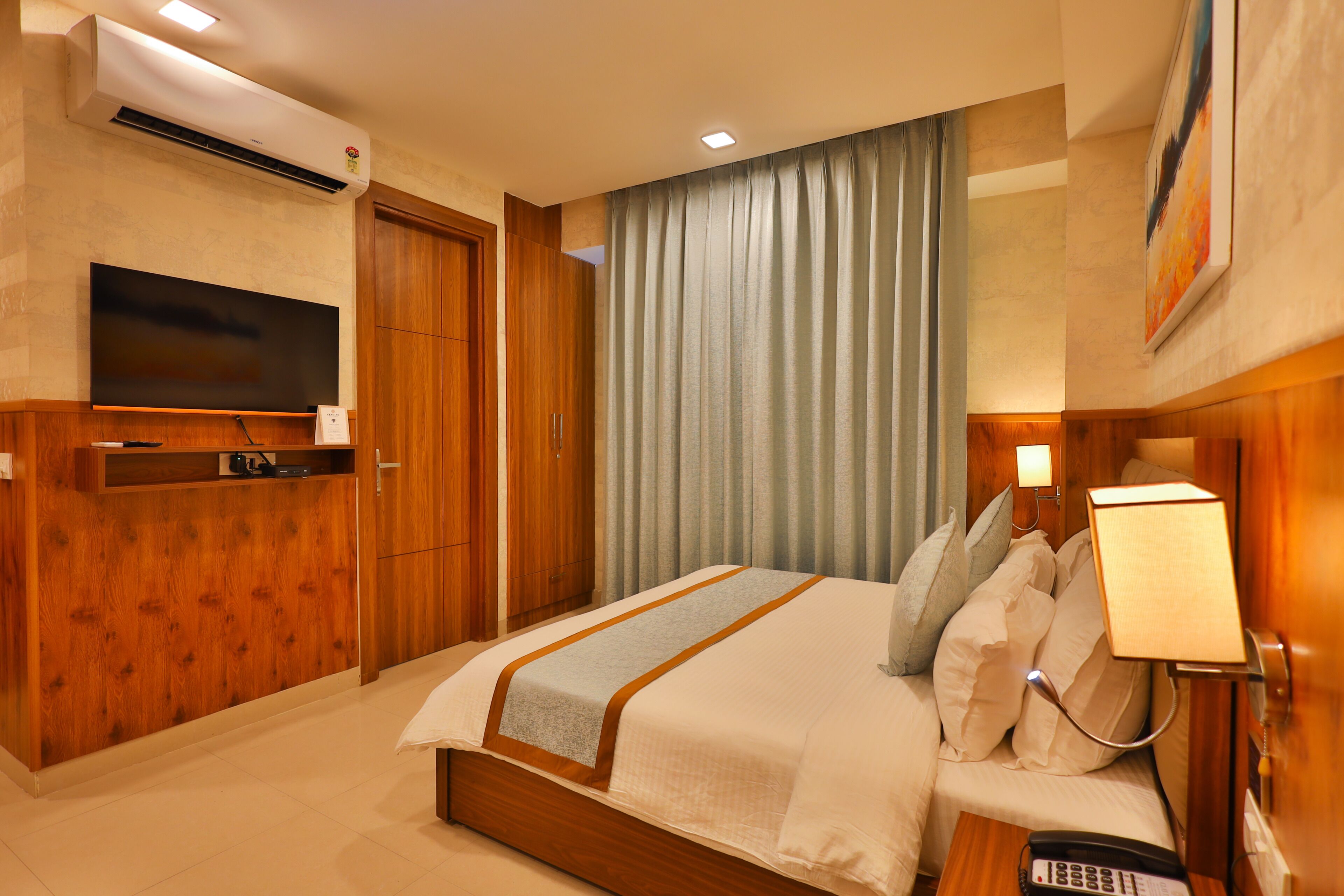 Quarto de hotel com cama, televisão na parede, mesa de cabeceira com abajur e telefone.