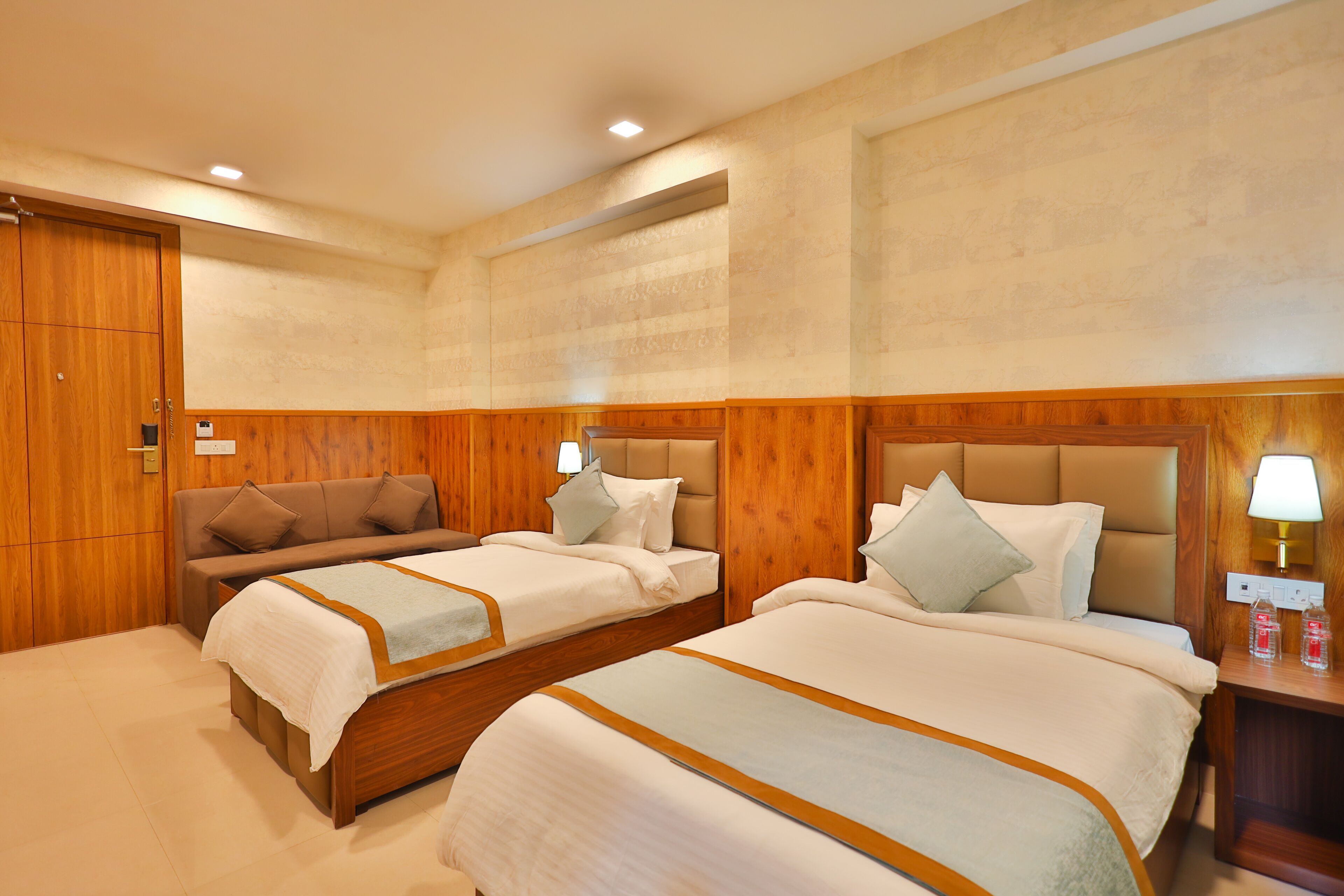 A hotel room with two beds, wooden paneling, and a nightstand with a lamp.