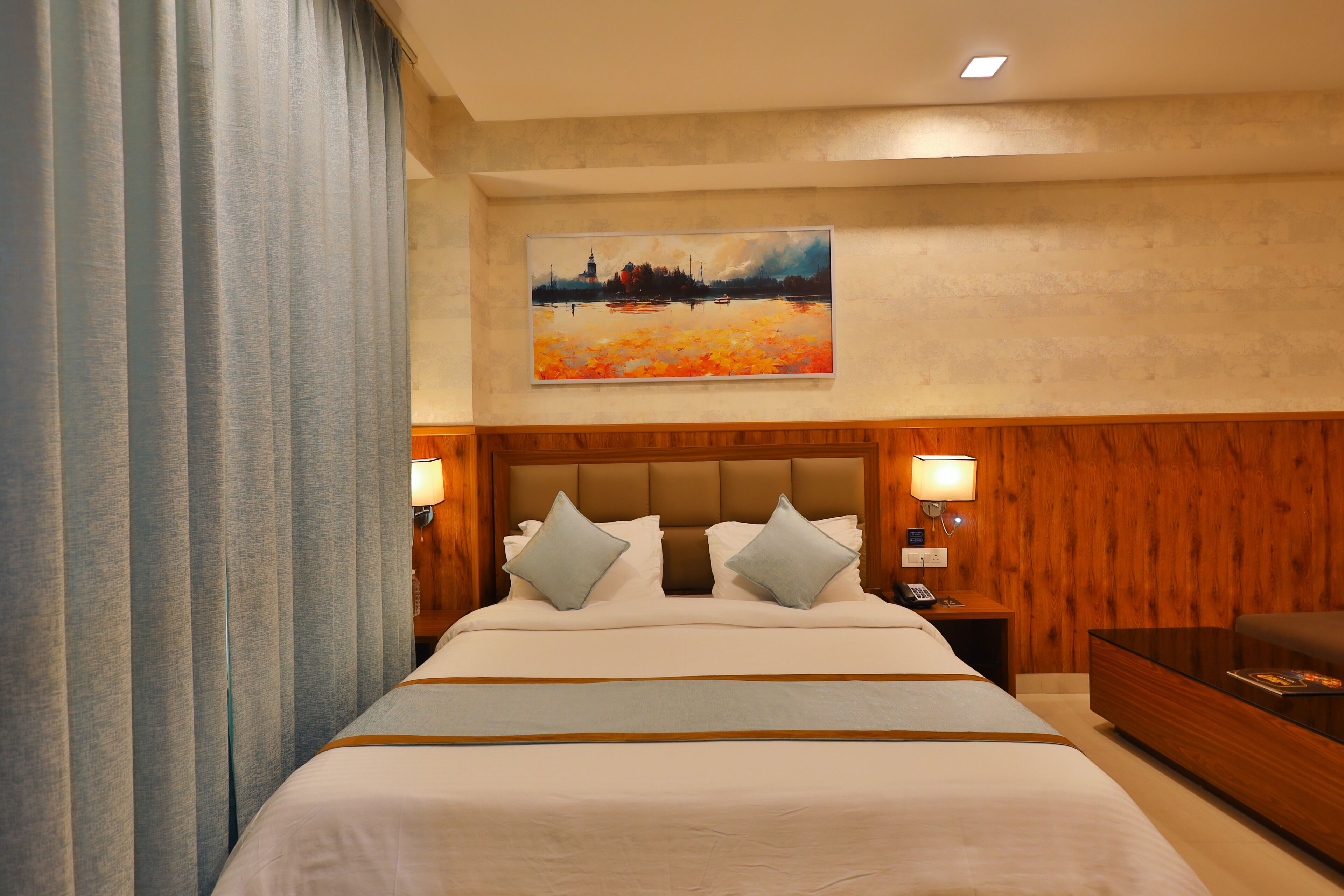 A hotel room with a large bed, wooden headboard, two bedside lamps, a painting on the wall, and a wooden nightstand.
