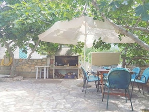 Eine Terrasse im Freien mit Grill, Stühlen und Tisch unter einem Baum.