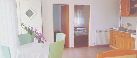 A room with a bed, a table with chairs, a radiator, and a door leading to another room.