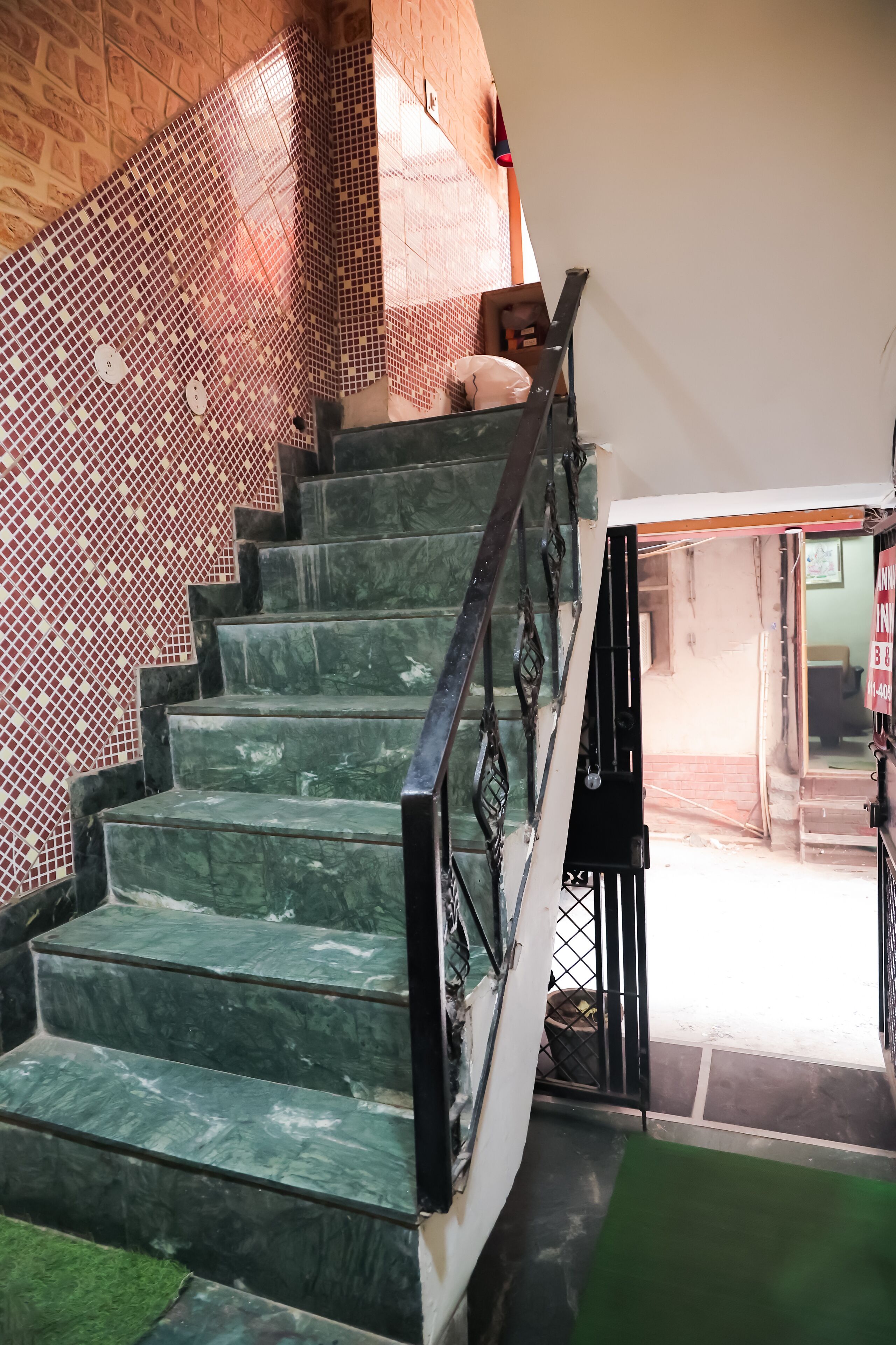 Una escalera con escalones de mármol verde y barandilla negra, que conduce a una habitación con pared de azulejos y una puerta.