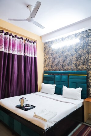 A neatly made bed with white linens, a teal headboard, and a small bedside table with a tray containing a coffee pot and a glass. - Roomshala 155 Hotel JPC (New Delhi)