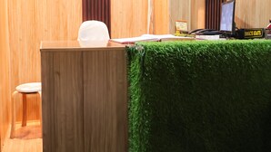 A reception area with a wooden desk, a white chair, and a green artificial grass barrier. There are signs on the wall, including one that says "MANNAT INN" and another that says "VISITORS ARE NOT ALLOWED." - Roomshala 155 Hotel JPC (New Delhi)