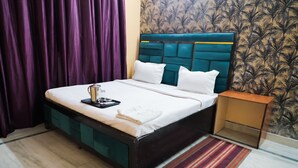 A neatly made bed with white linens and pillows, a bedside table with a tray, and a patterned wall. - Roomshala 155 Hotel JPC (New Delhi)