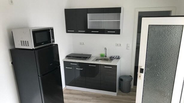 Een compacte keuken met een zwarte koelkast, een magnetron, een spoelbak en een klein aanrecht.