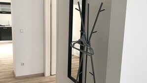 Een gang met een houten vloer, een spiegel met zwart frame leunt tegen de muur, en een deur die leidt naar een keuken.