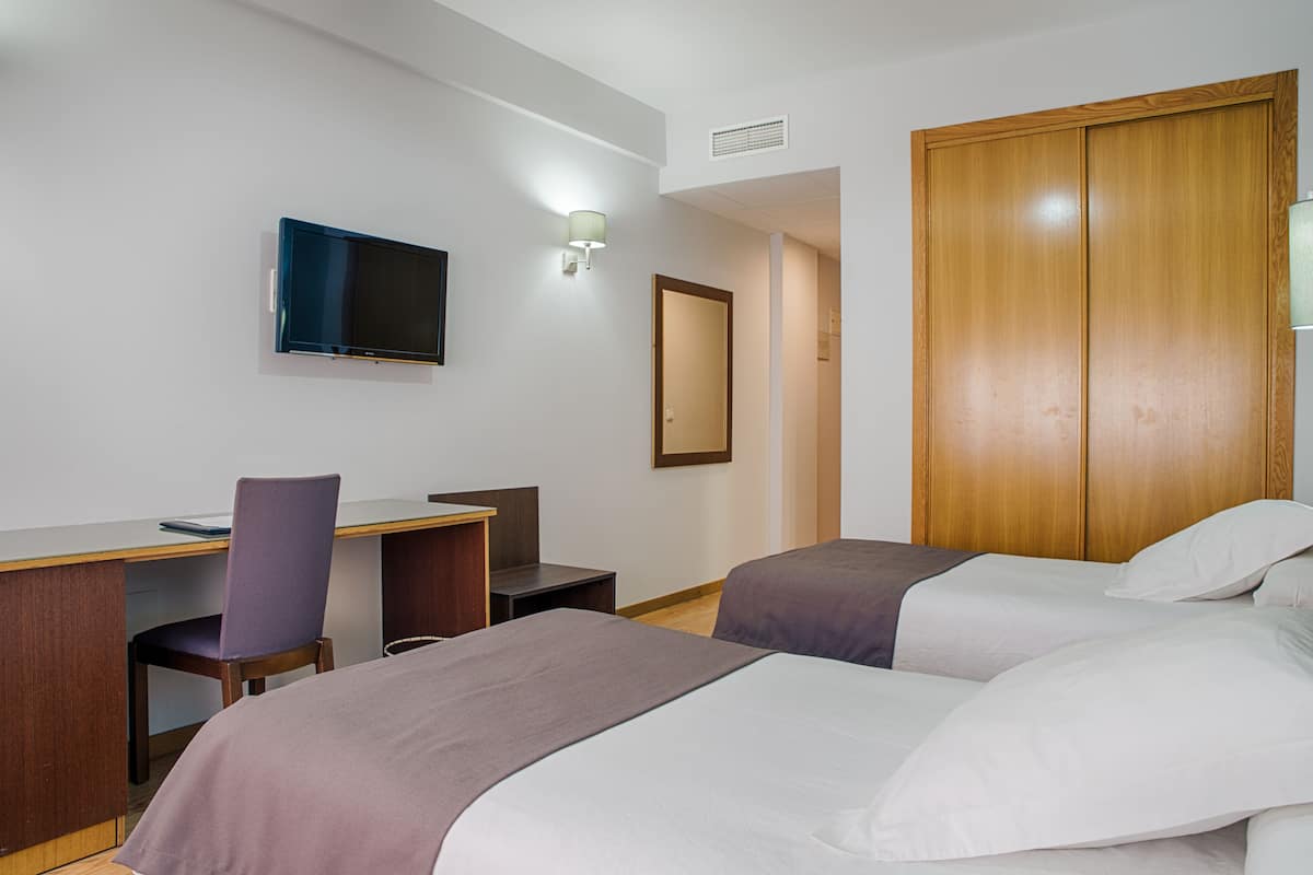 A hotel room with two beds, a desk, a chair, a television, and a wardrobe.