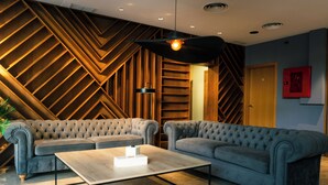 Un intérieur moderne avec un canapé d’angle, une table basse et un mur orné d’un motif géométrique.