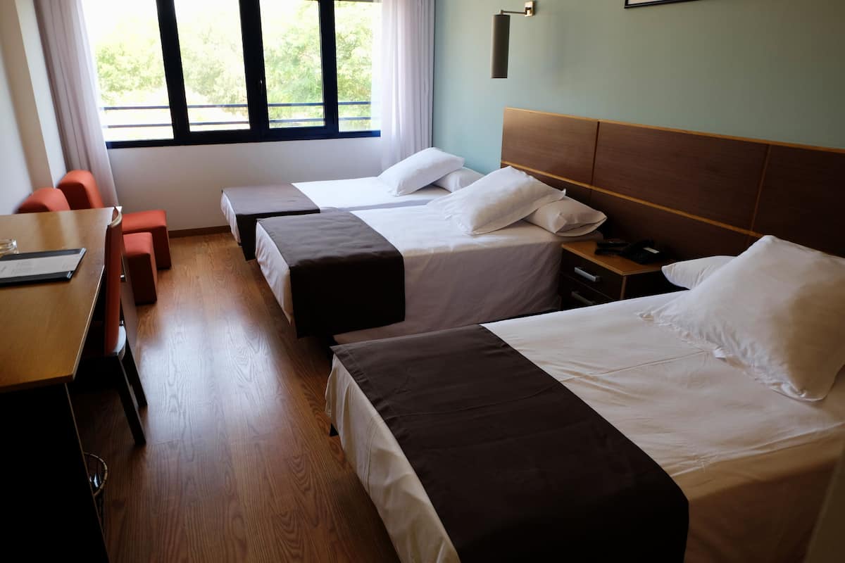 A hotel room with two beds, a wooden desk, and a window with curtains.