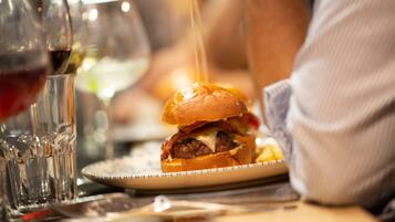 Close-up van een hamburger met broodje, kaas en saus die erop gegoten wordt, op een bord geplaatst.