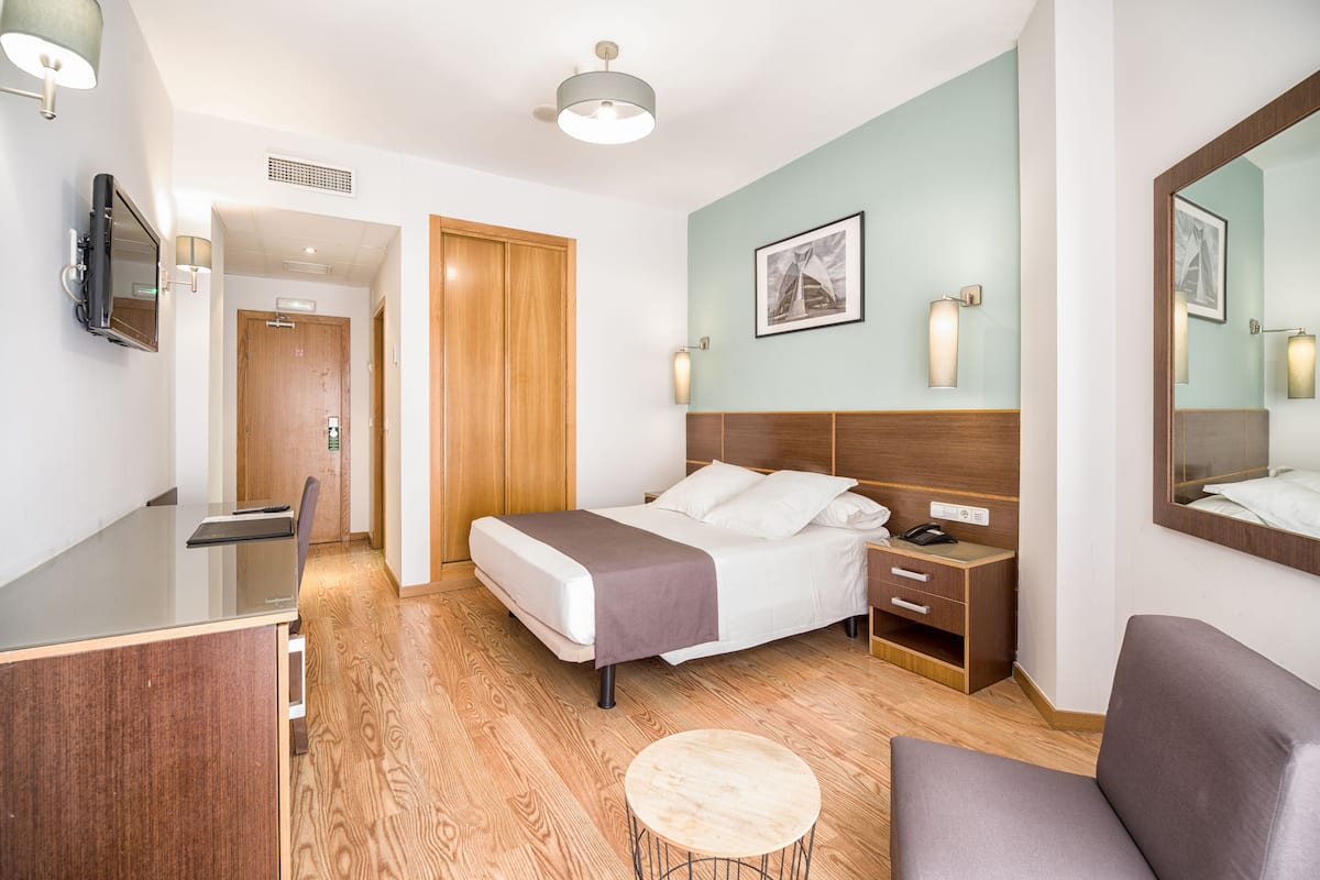 A hotel room with a bed, bedside table, chair, desk, and a round table.