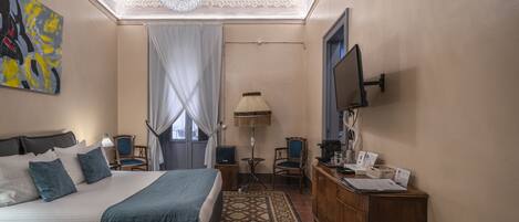 A hotel room with a large bed, a desk with a computer, a television, a lamp, and a painting on the wall.