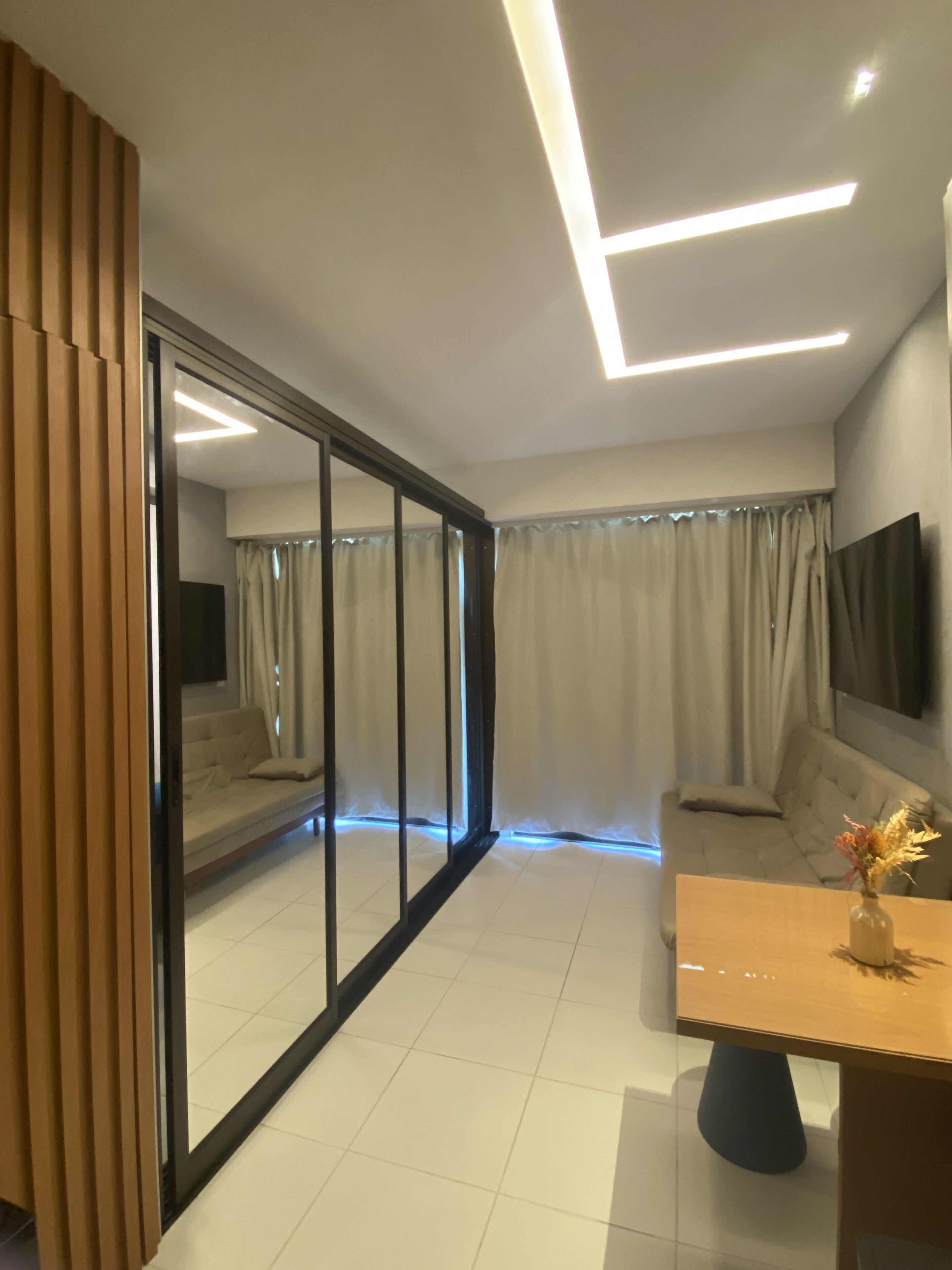 Un salon moderne doté d’une porte-fenêtre coulissante, d’un canapé, d’une table basse et d’un téléviseur à écran plat fixé au mur.