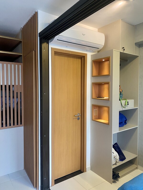 Una habitación moderna con puerta de madera, estanterías empotradas y aire acondicionado instalado en el techo.