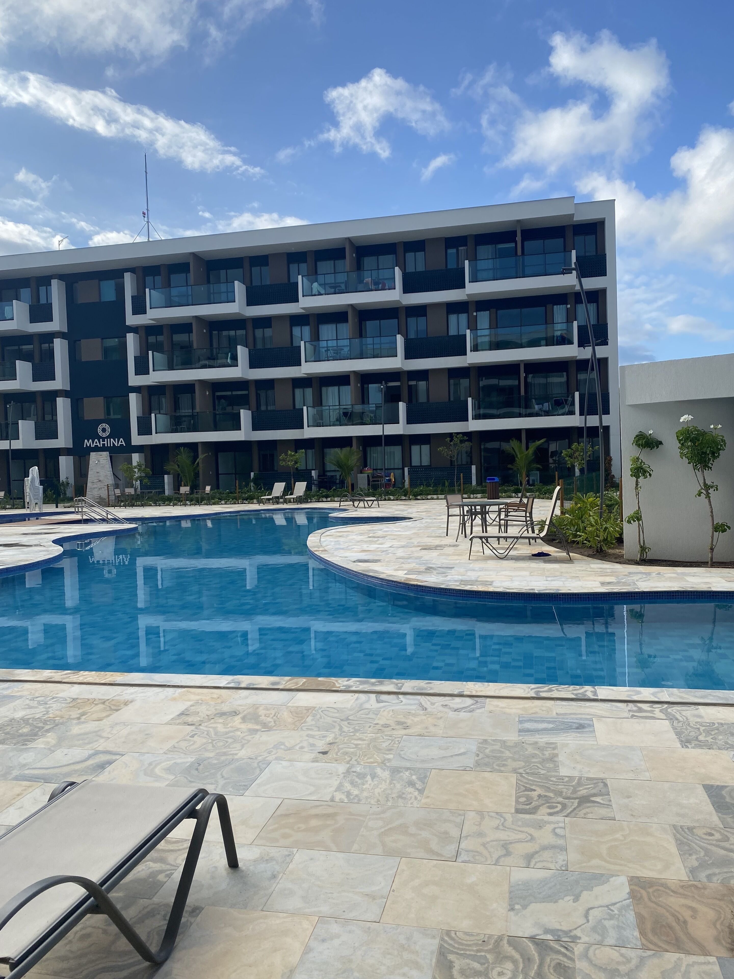 A modern building with a swimming pool, outdoor seating, and a clear sky.