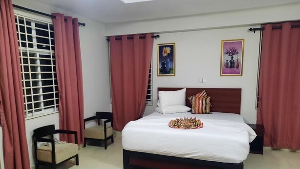 A bedroom with a bed, a chair, a small table, and two framed pictures on the wall. - EFUA ANOAH HOTEL & APARTMENT (Sekondi-Takoradi)