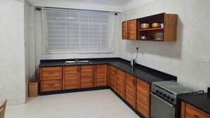 A kitchen with wooden cabinets, a black countertop, a stove, and a window with a grid pattern. - EFUA ANOAH HOTEL & APARTMENT (Sekondi-Takoradi)