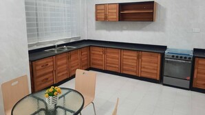 A kitchen with wooden cabinets, a gas stove, and a glass table with chairs. - EFUA ANOAH HOTEL & APARTMENT (Sekondi-Takoradi)