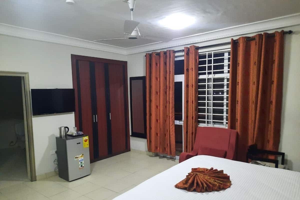 Une chambre d’hôtel comprenant un lit, un bureau avec une bouilloire, une armoire et une fenêtre avec des rideaux.