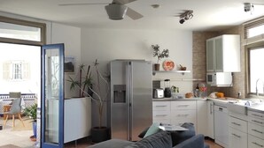 Een moderne keuken met een koelkast, magnetron en fornuis. Er is een eethoek met een tafel en stoelen, en een bank in de woonkamer.