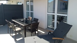 An outdoor patio with a glass table and chairs, a dark-colored lounge chair, and a white wall with a window. - Apartment "luka" (Vodice)