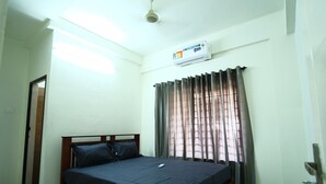 Quarto com cama, ventilador de teto, aparelho de ar condicionado e janela com cortinas.