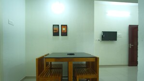 Uma sala de jantar com uma mesa de madeira e quatro cadeiras, uma televisão de tela plana na parede e uma porta à direita.