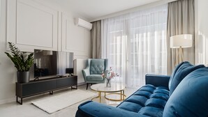 Ein modernes Wohnzimmer mit einem blauen Sofa, einem Fernseher, einem Sessel und einer Stehlampe.