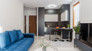 Ein modernes Wohnzimmer mit blauem Sofa, einer Küchenzeile mit Bar und einem Fernseher auf der rechten Seite.