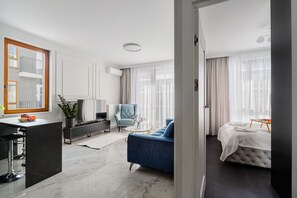 Een moderne hotelkamer met een marmeren vloer, een blauwe bank, een bed met een witte dekbedovertrek, een klein rond tafeltje en een televisie.