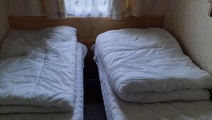 A room with two single beds, a wooden headboard, and a window with sheer curtains. - Beautiful 3-bed Static Caravan in Skegness (Skegness)
